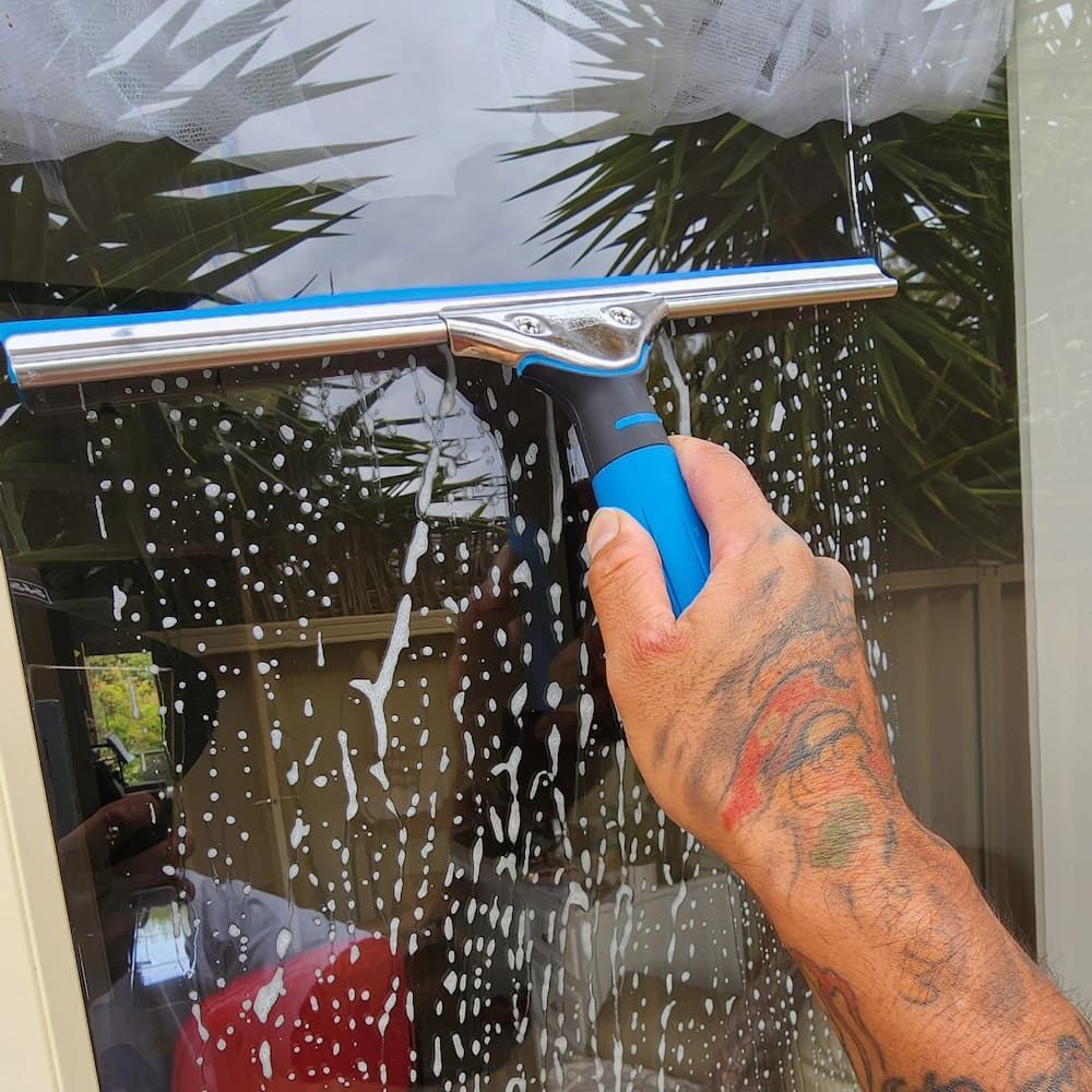 A Person With Tattoos Using a Squeegee to Clean a Soapy Window — Rapid Rinse Solutions in Cobram, VIC