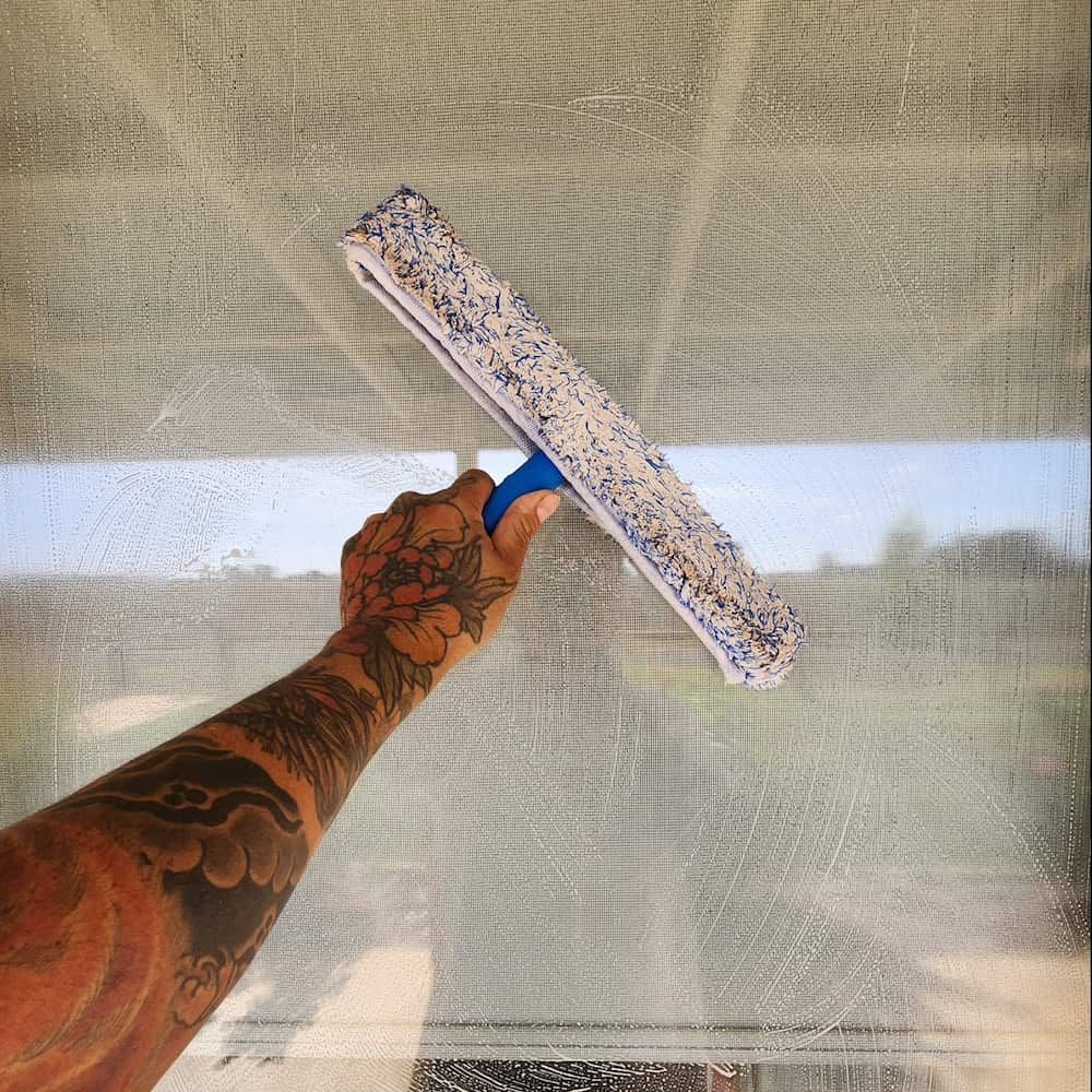 A Person With Tattoos is Using a Squeegee to Clean a Window — Rapid Rinse Solutions in Cobram, VIC