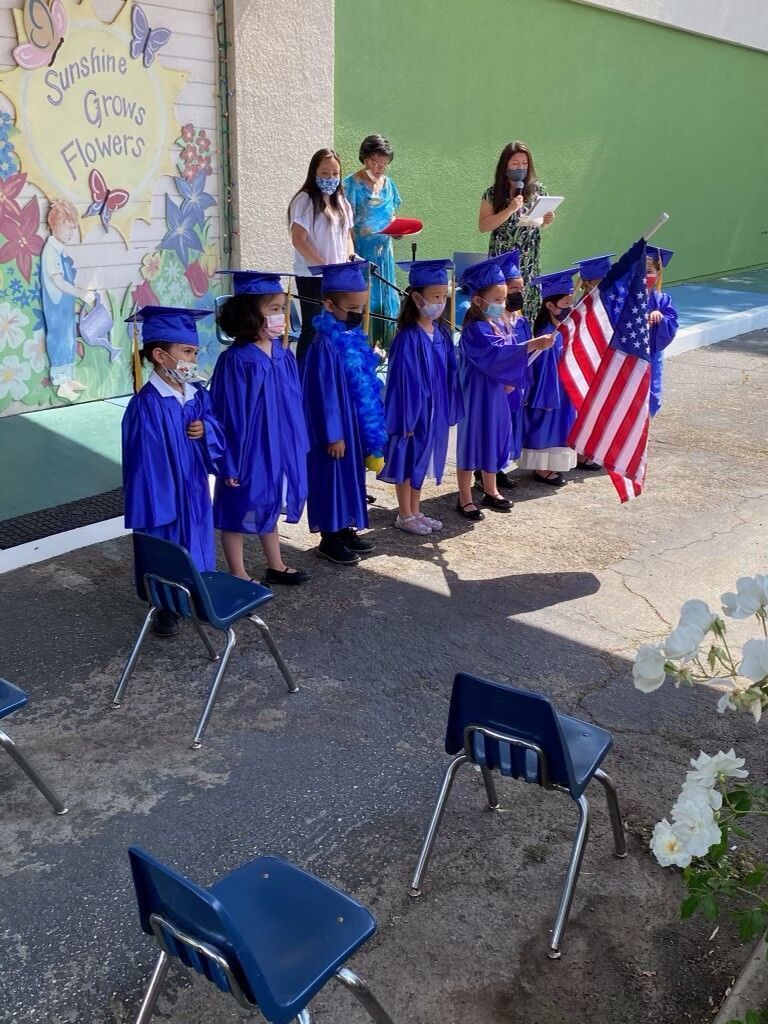 A group of children wearing graduation caps and gowns are standing in front of a building.