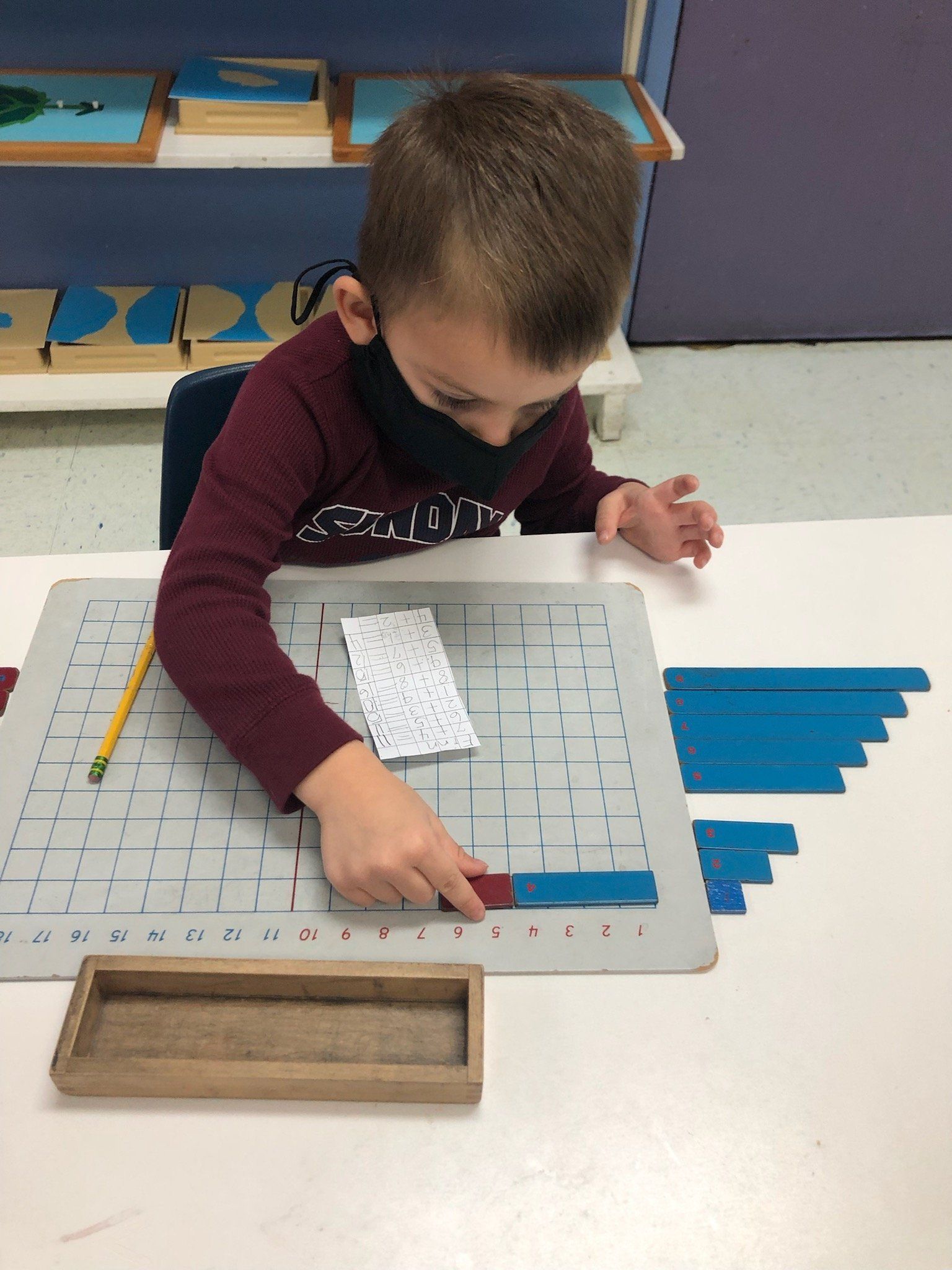 A young boy wearing a mask is sitting at a table playing with blocks.