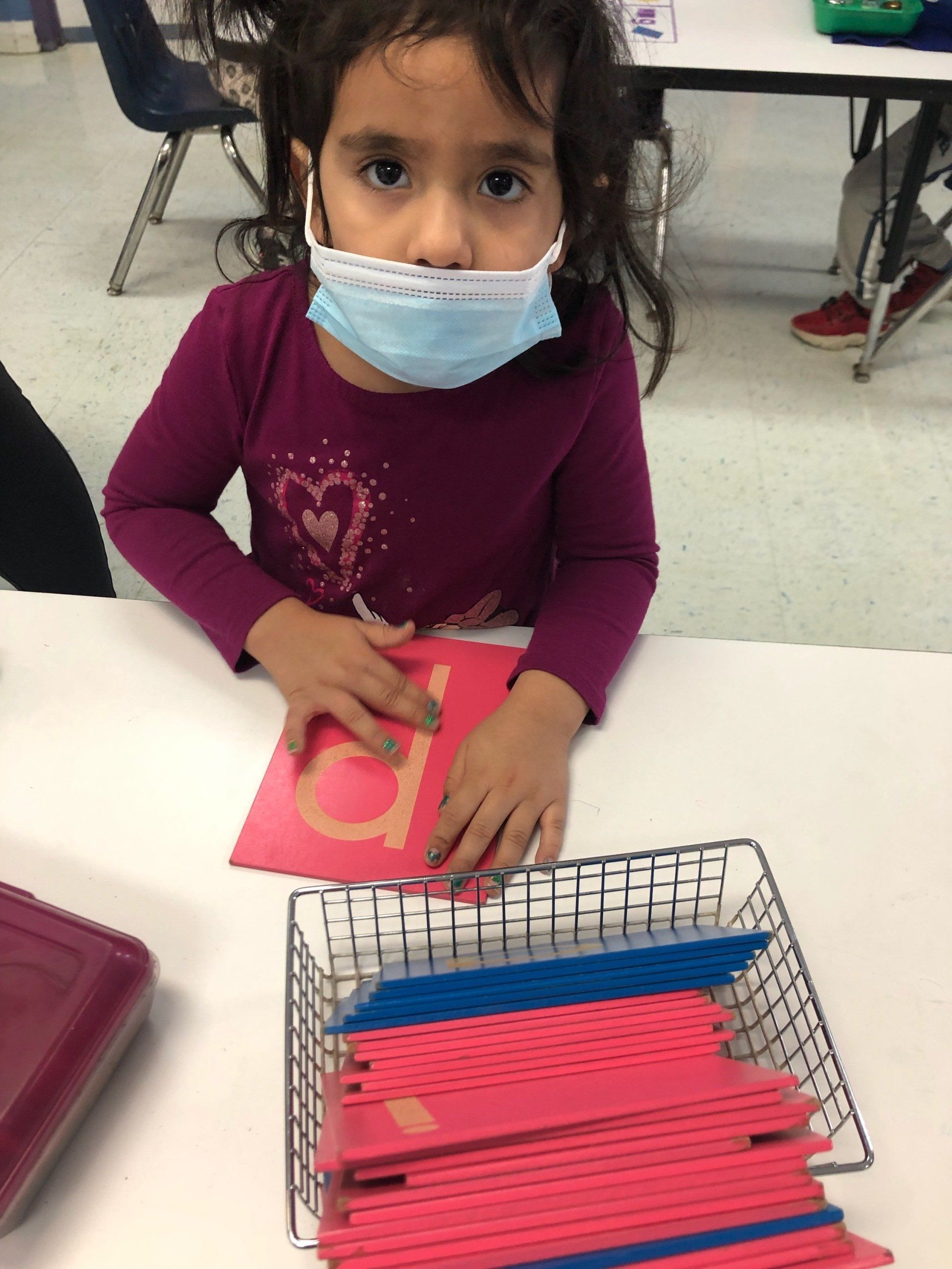 A little girl wearing a mask is sitting at a table