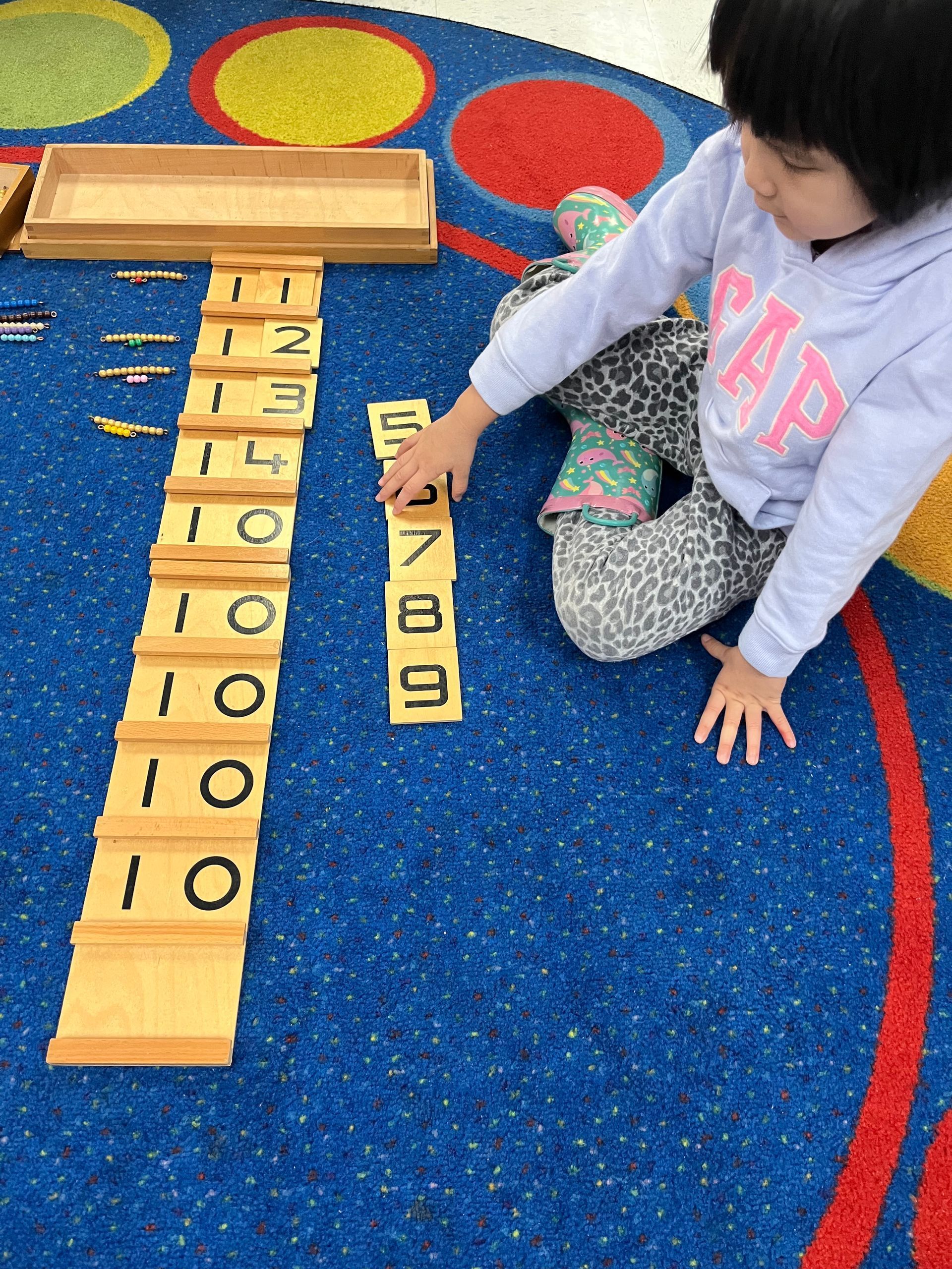 A little girl wearing a gap sweatshirt is playing with numbers on the floor