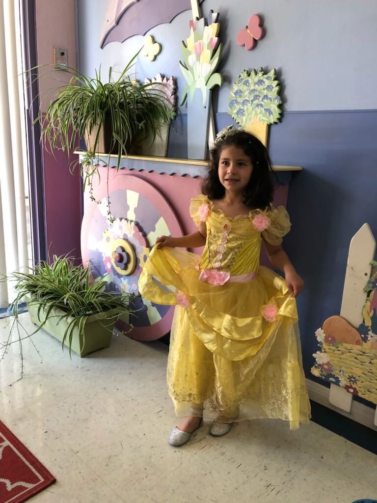 A little girl in a yellow princess dress is standing in a room.