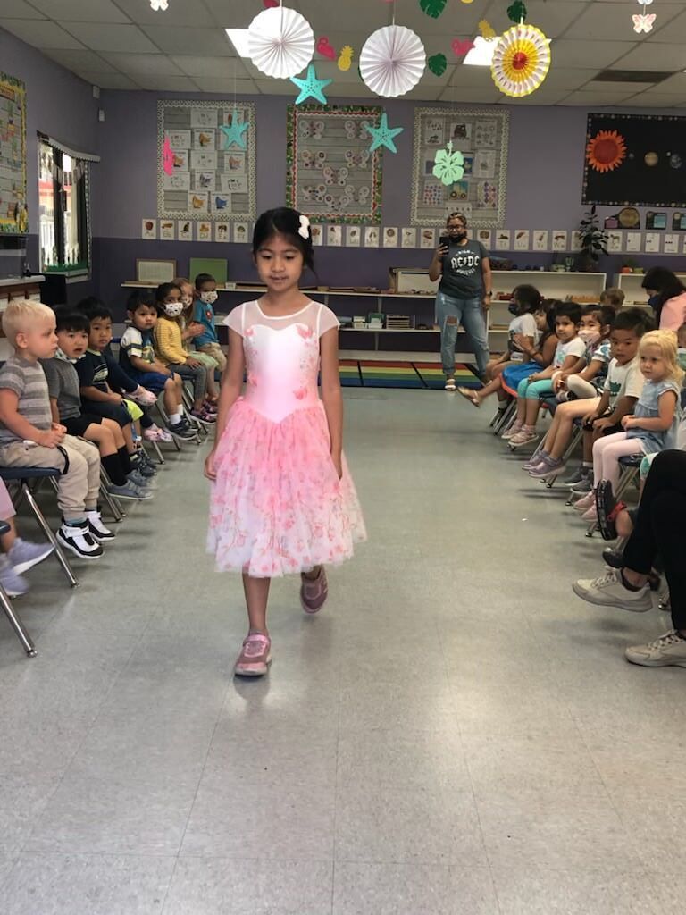 A little girl in a pink dress is walking down a runway in front of a group of children.