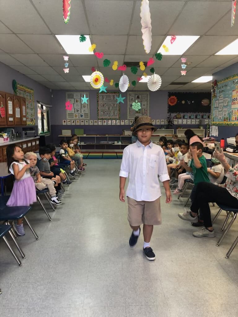 A boy wearing a hat is walking through a classroom filled with children.