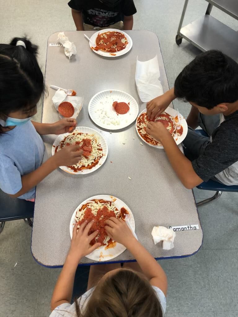A group of children are sitting at a table making pizzas.