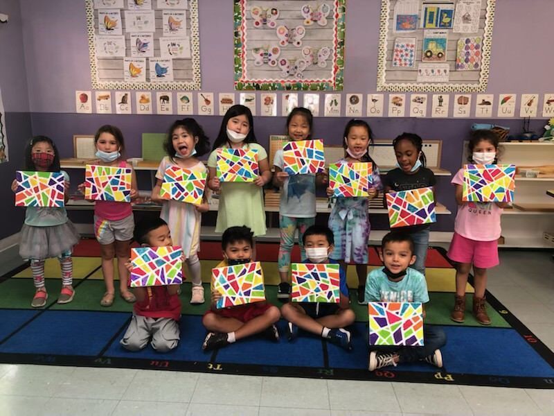 A group of children are holding up their artwork in a classroom.