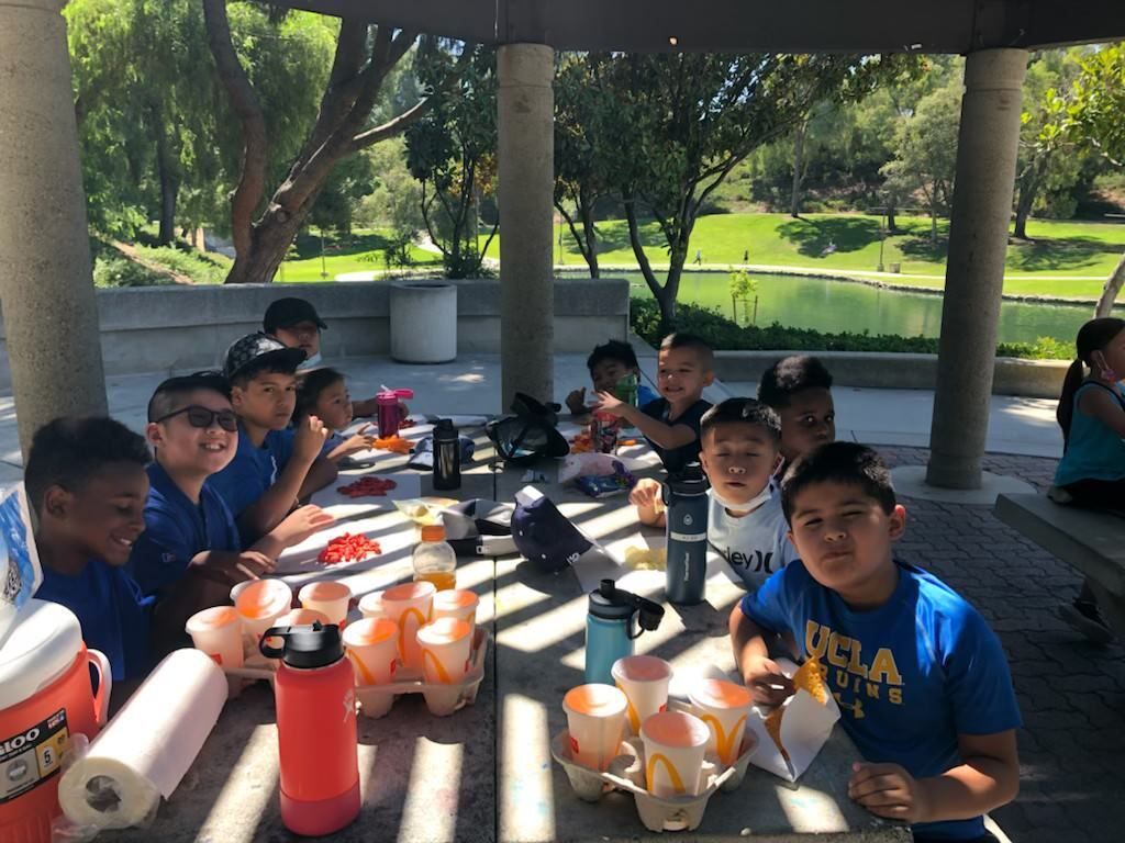 A group of children are sitting at a picnic table in a park.