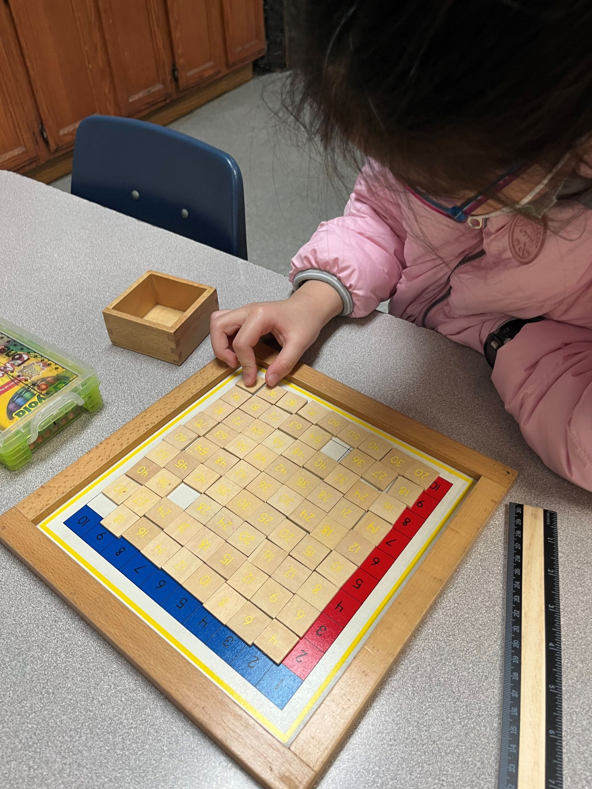 A little girl is playing with a wooden maze on a table.