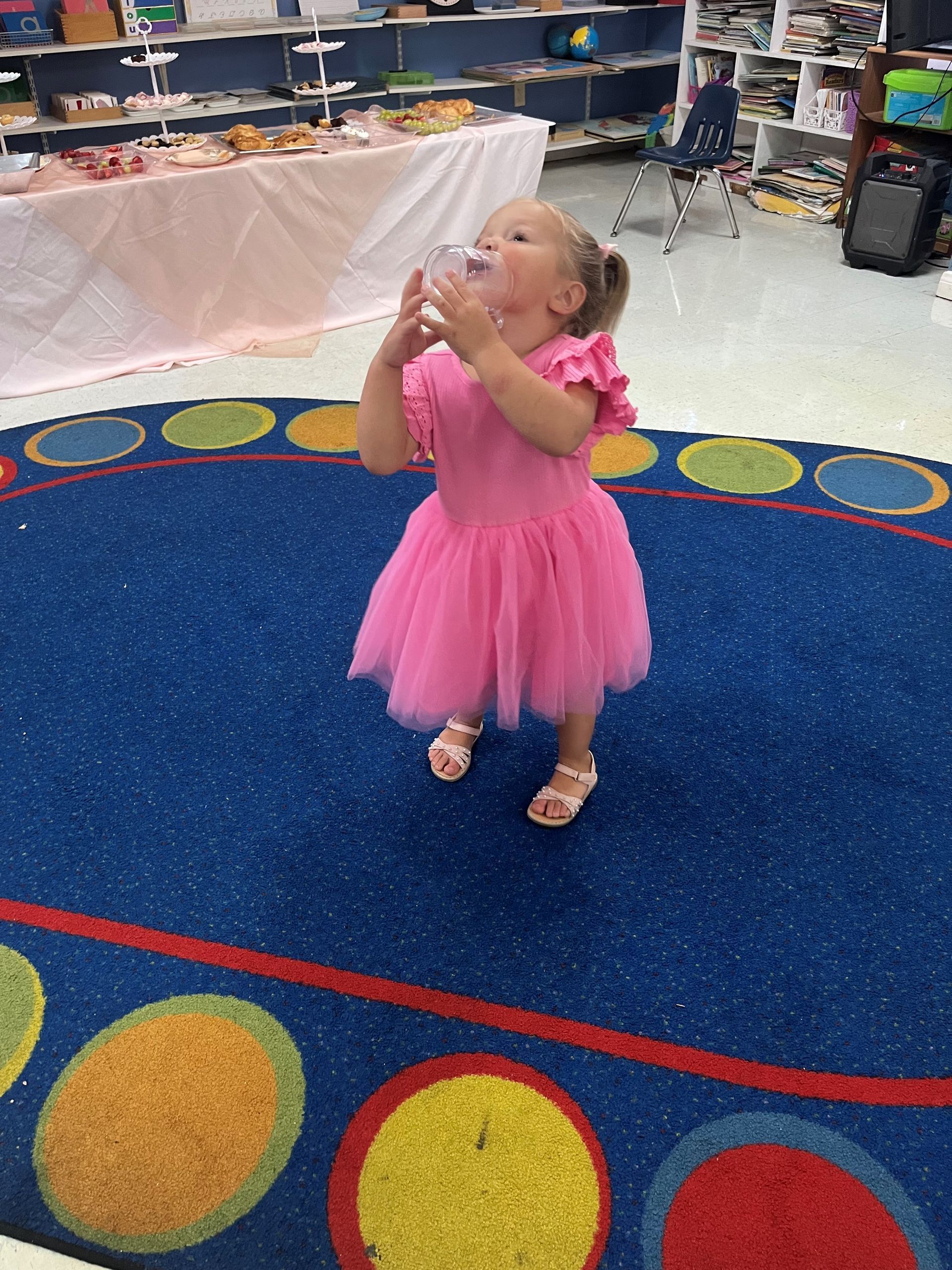 A little girl in a pink dress is standing on a blue rug