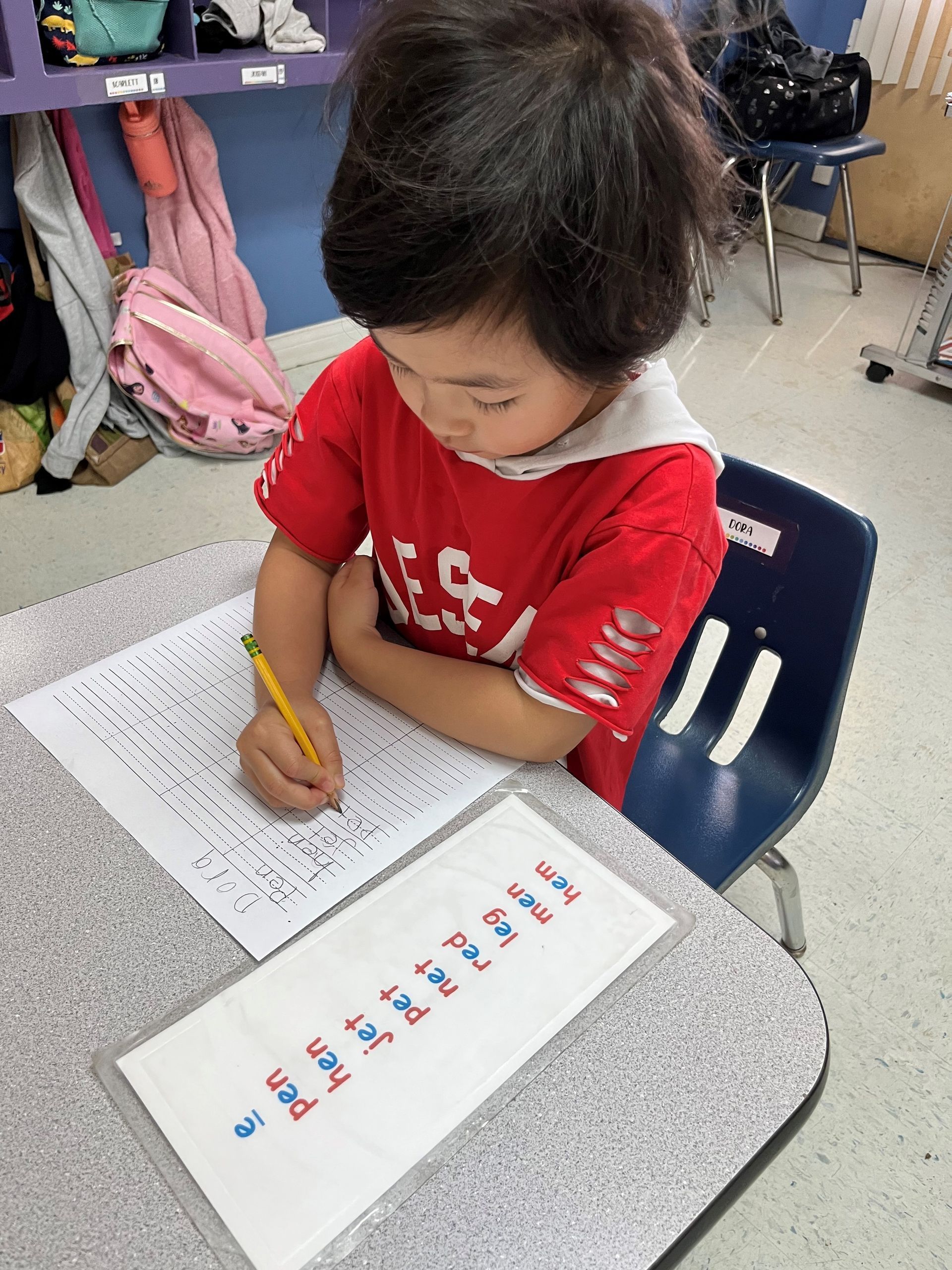 A young boy in a red shirt is writing on a piece of paper