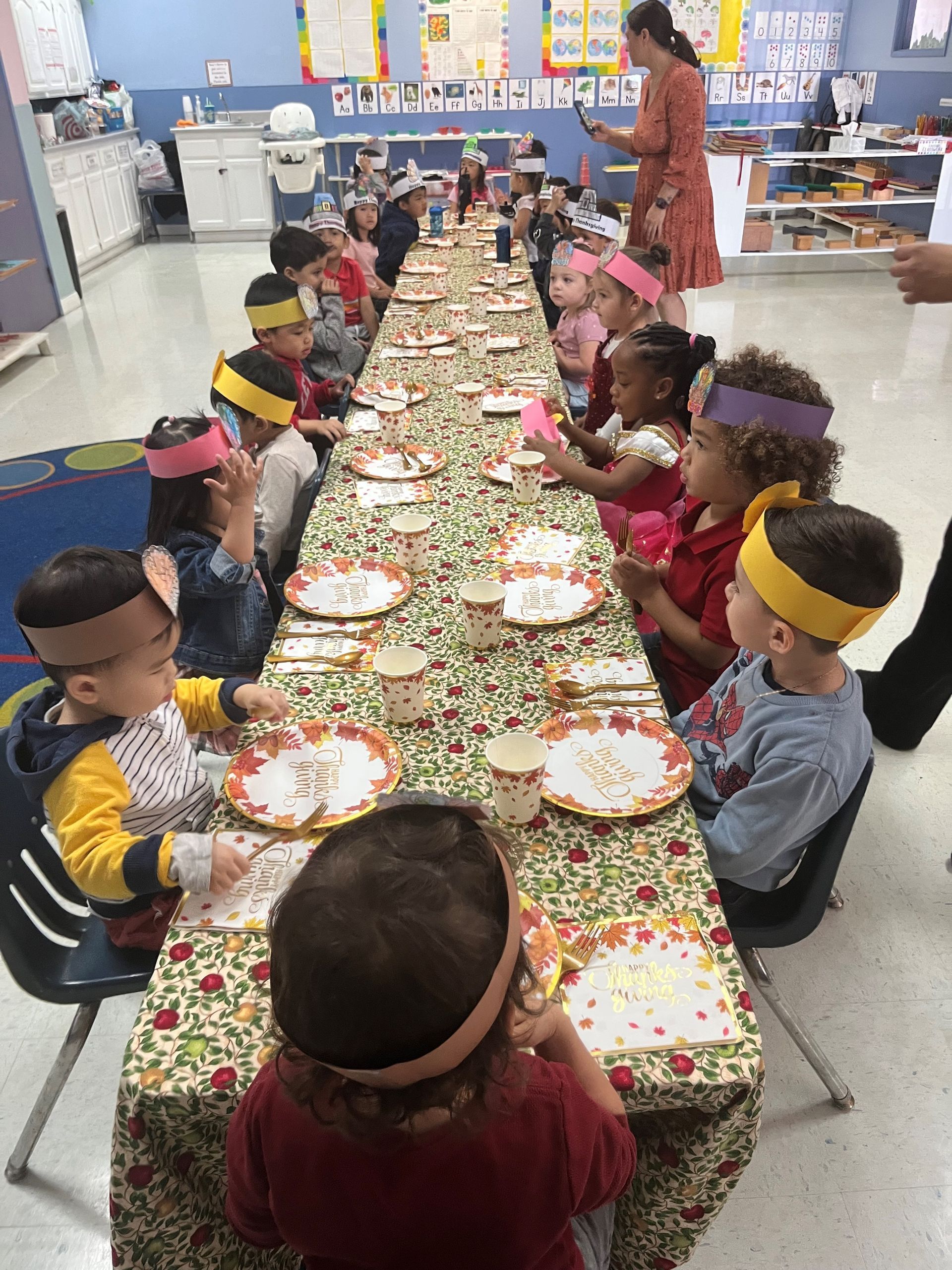 A group of children are sitting at a long table with plates and cups.