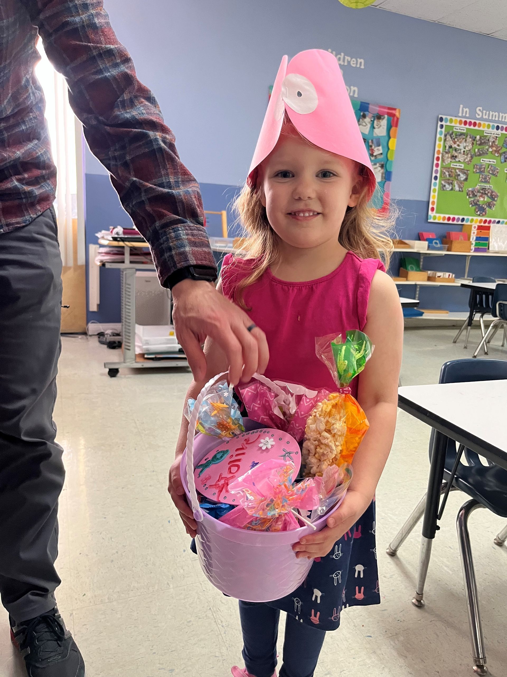 A little girl wearing a pink hat is holding a basket of candy.