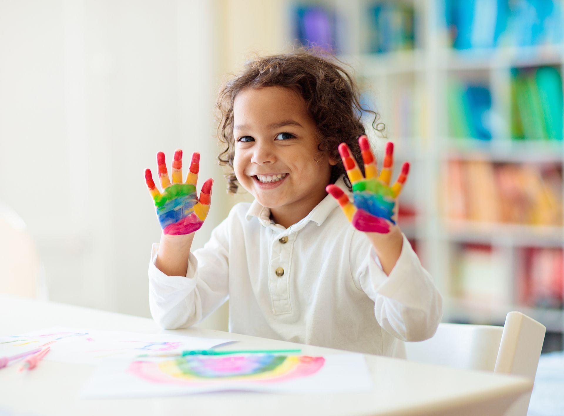 A little girl is sitting at a table with her hands painted in different colors.