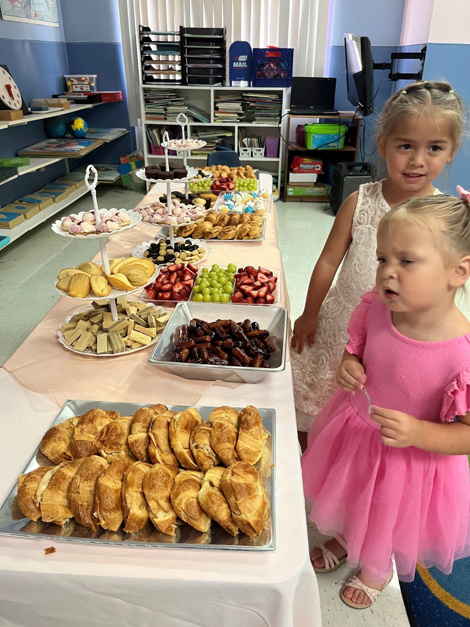 Two little girls are standing in front of a table full of food.