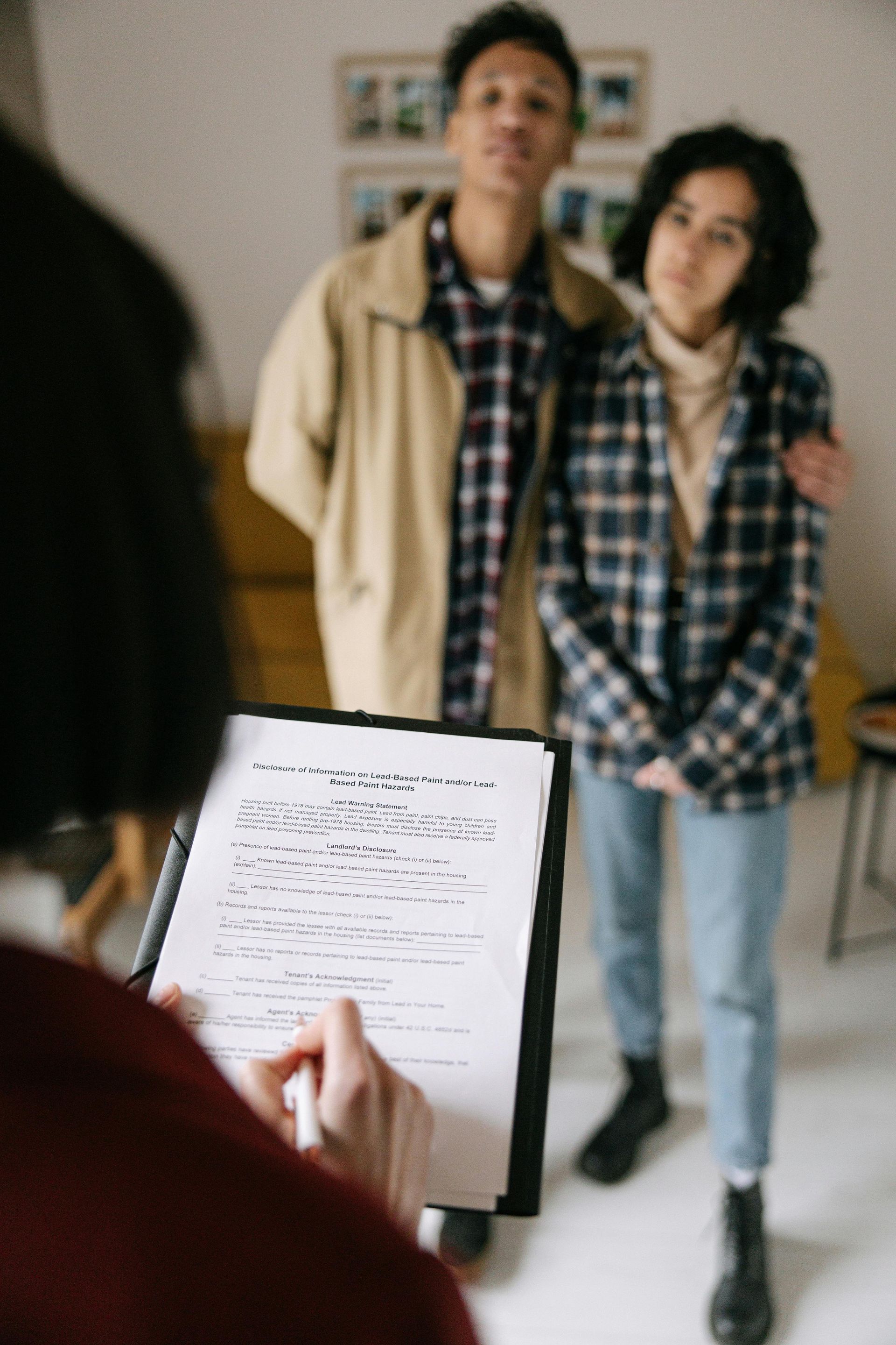 A man and a woman are standing in front of a woman holding a clipboard.