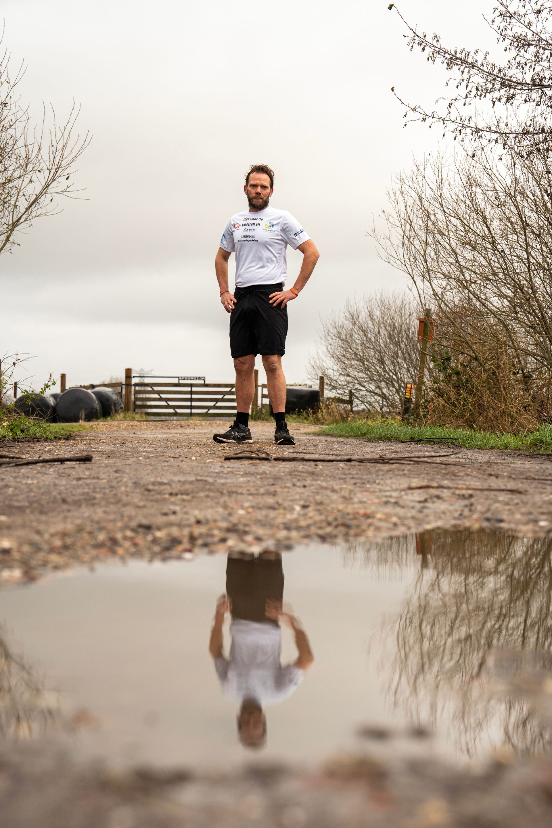 Een man staat in een plas water op een onverharde weg.