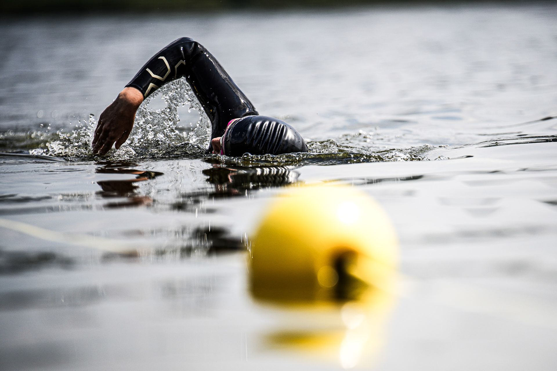 Een persoon zwemt in een meer met een gele boei op de voorgrond.