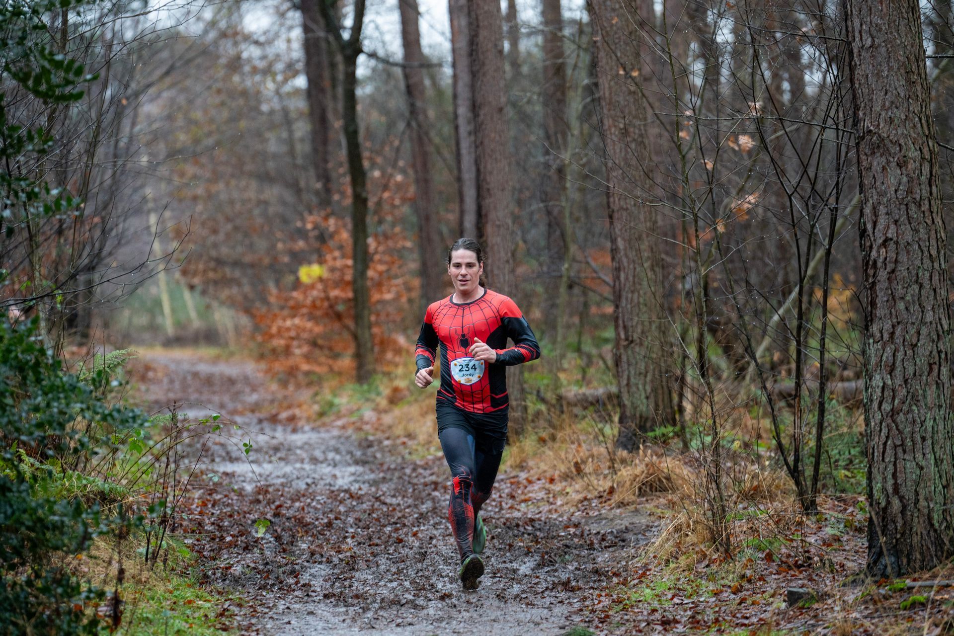 Een man rent over een modderig pad in het bos.