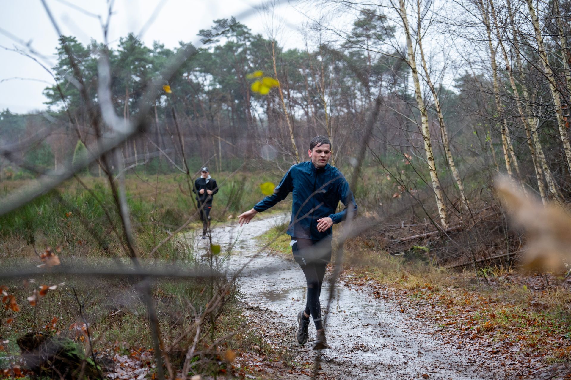 Een man rent over een modderig pad in het bos.