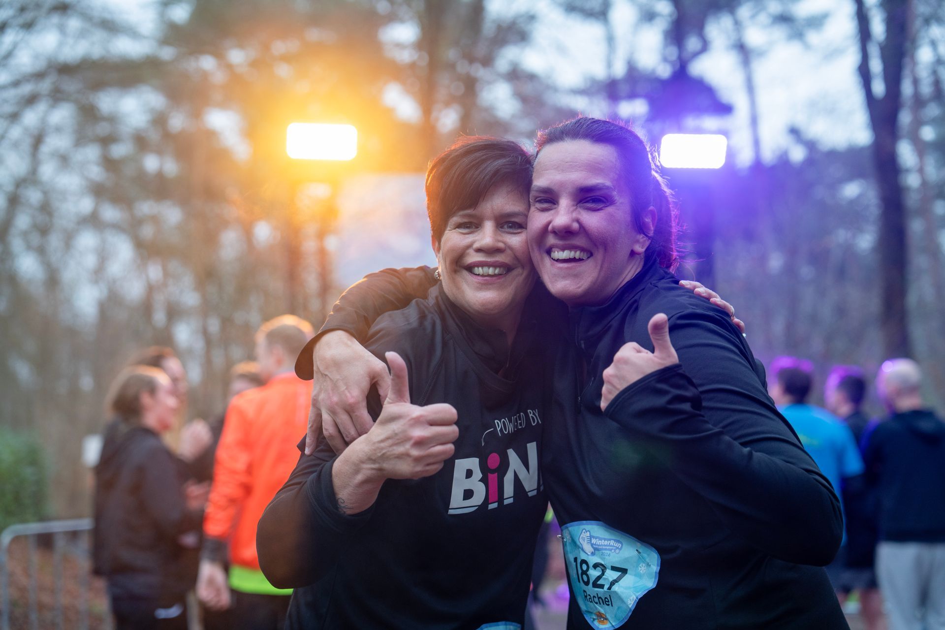 Twee vrouwen poseren voor een foto tijdens een race en steken hun duim omhoog.