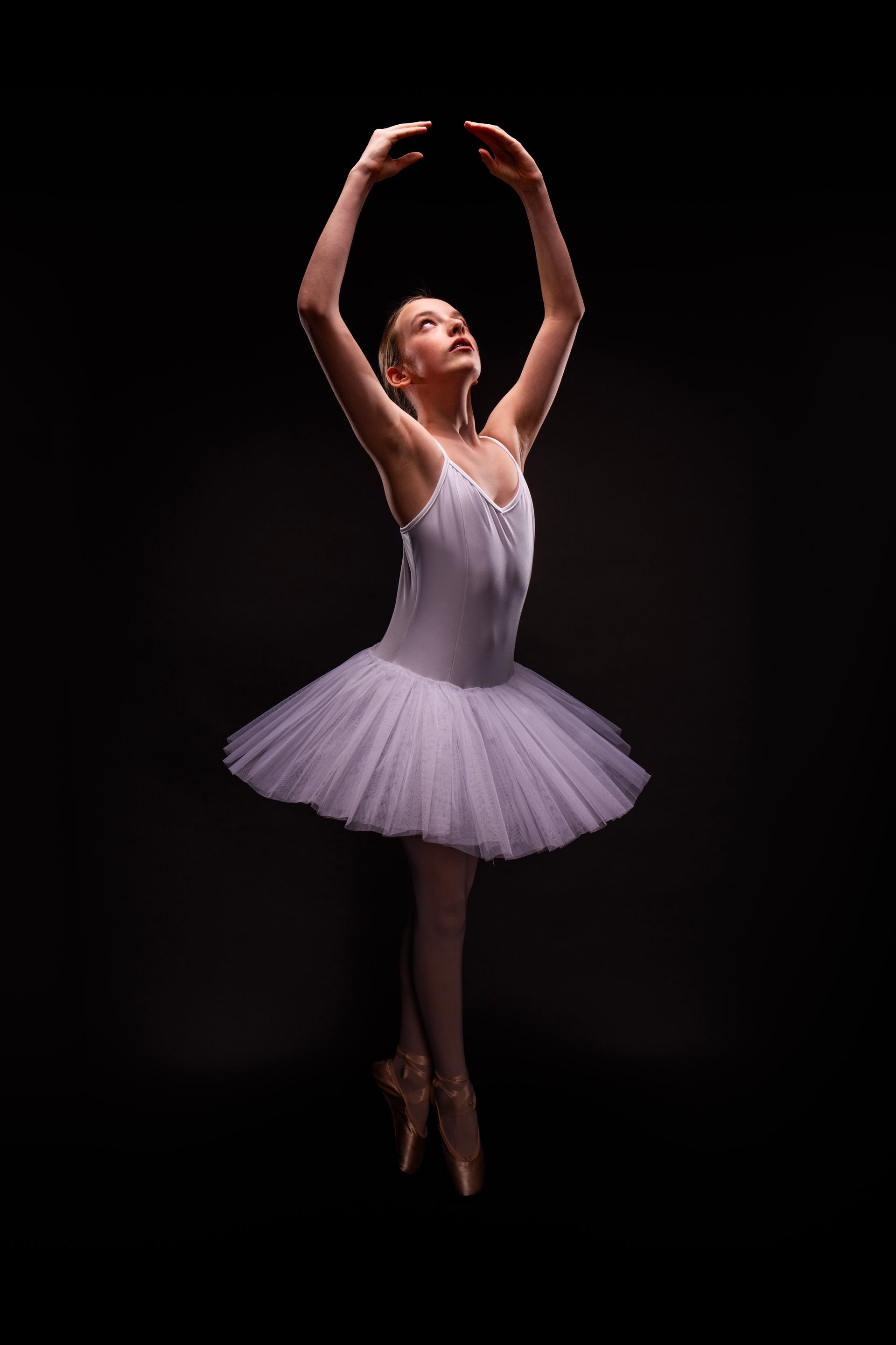 Een ballerina in een witte tutu en op puntschoenen danst op een zwarte achtergrond.