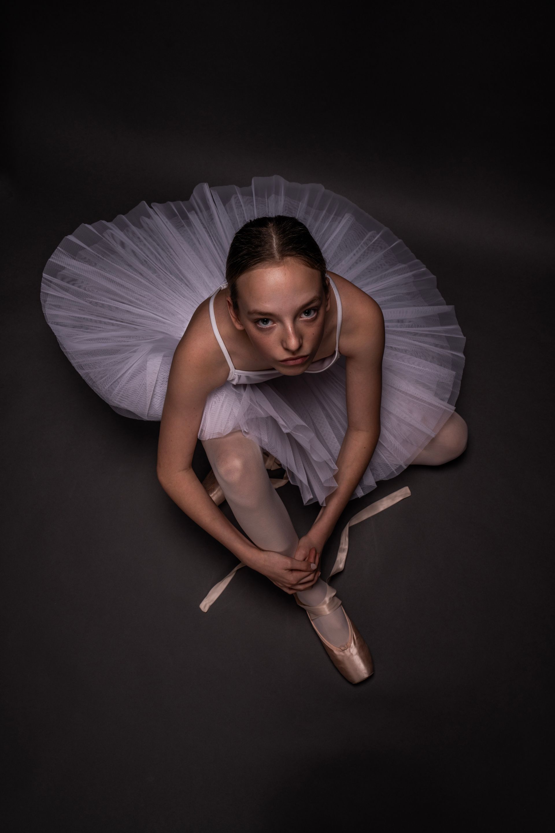 Een ballerina zit op de grond en strikt haar schoenen.