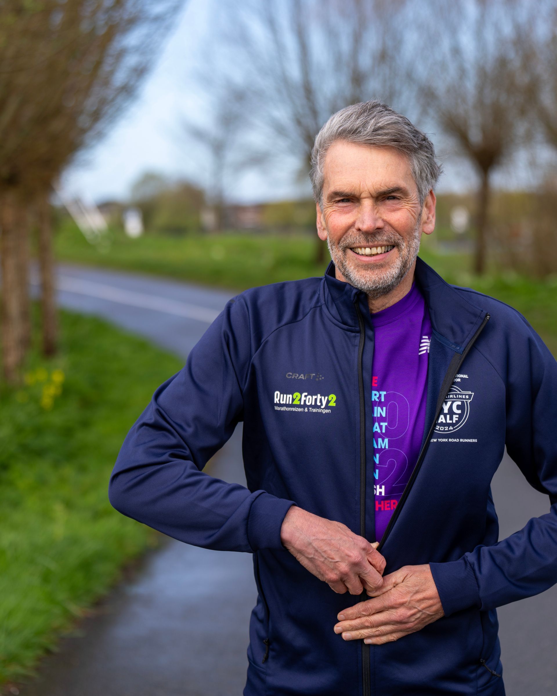 Een man met een baard draagt een blauw jasje en een paars shirt.