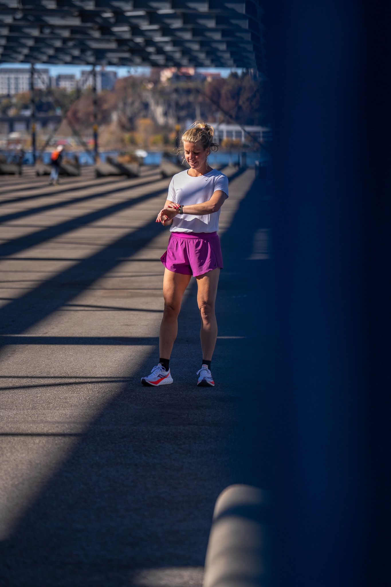 Een vrouw in een paarse korte broek en een wit shirt staat op een brug.