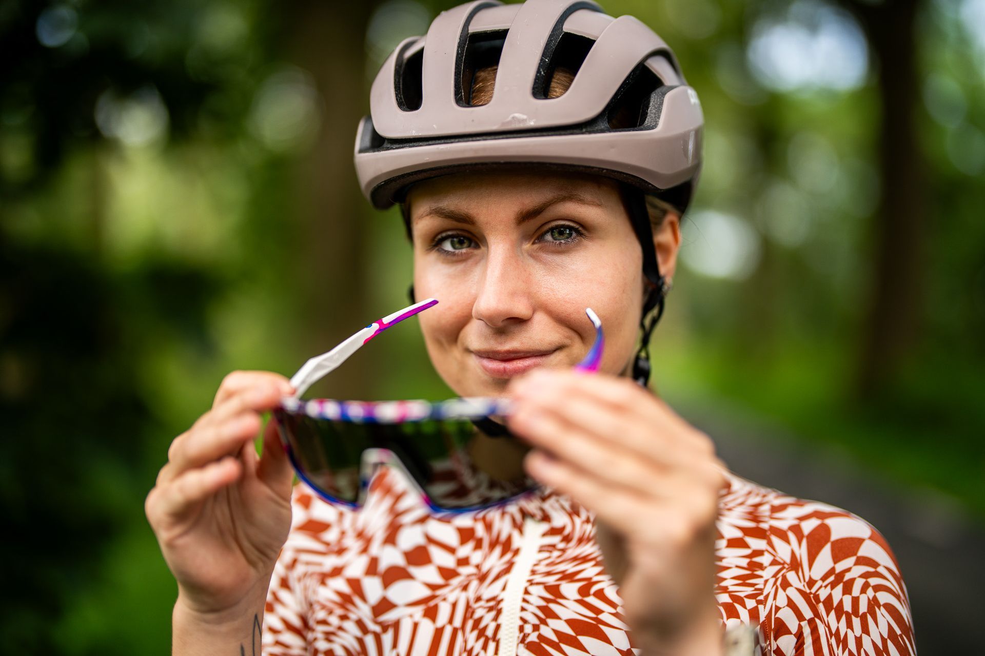 Een vrouw met een helm en een zonnebril houdt een zonnebril vast.
