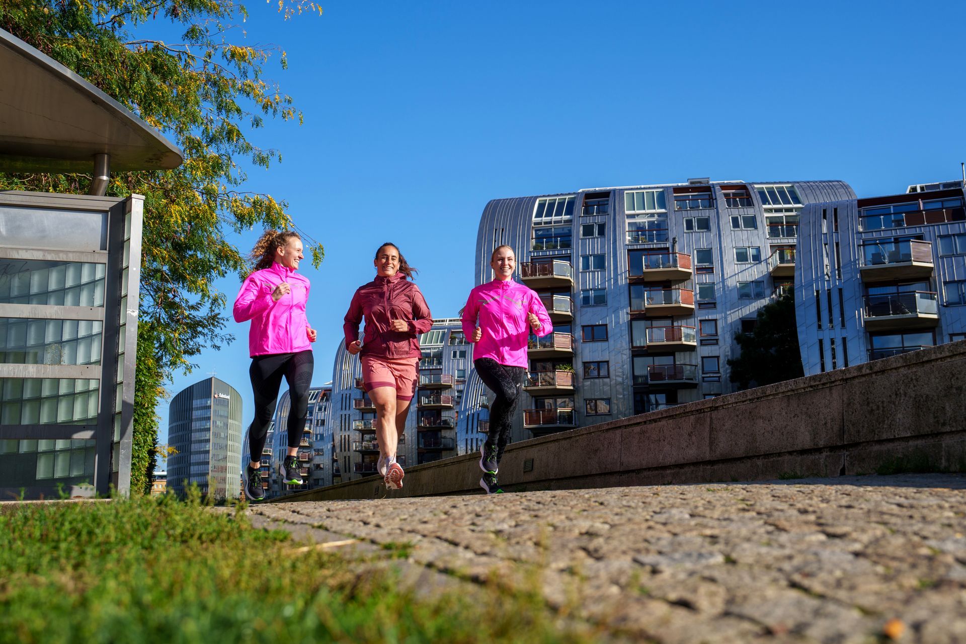 Drie vrouwen rennen over een geplaveide straat voor een gebouw.