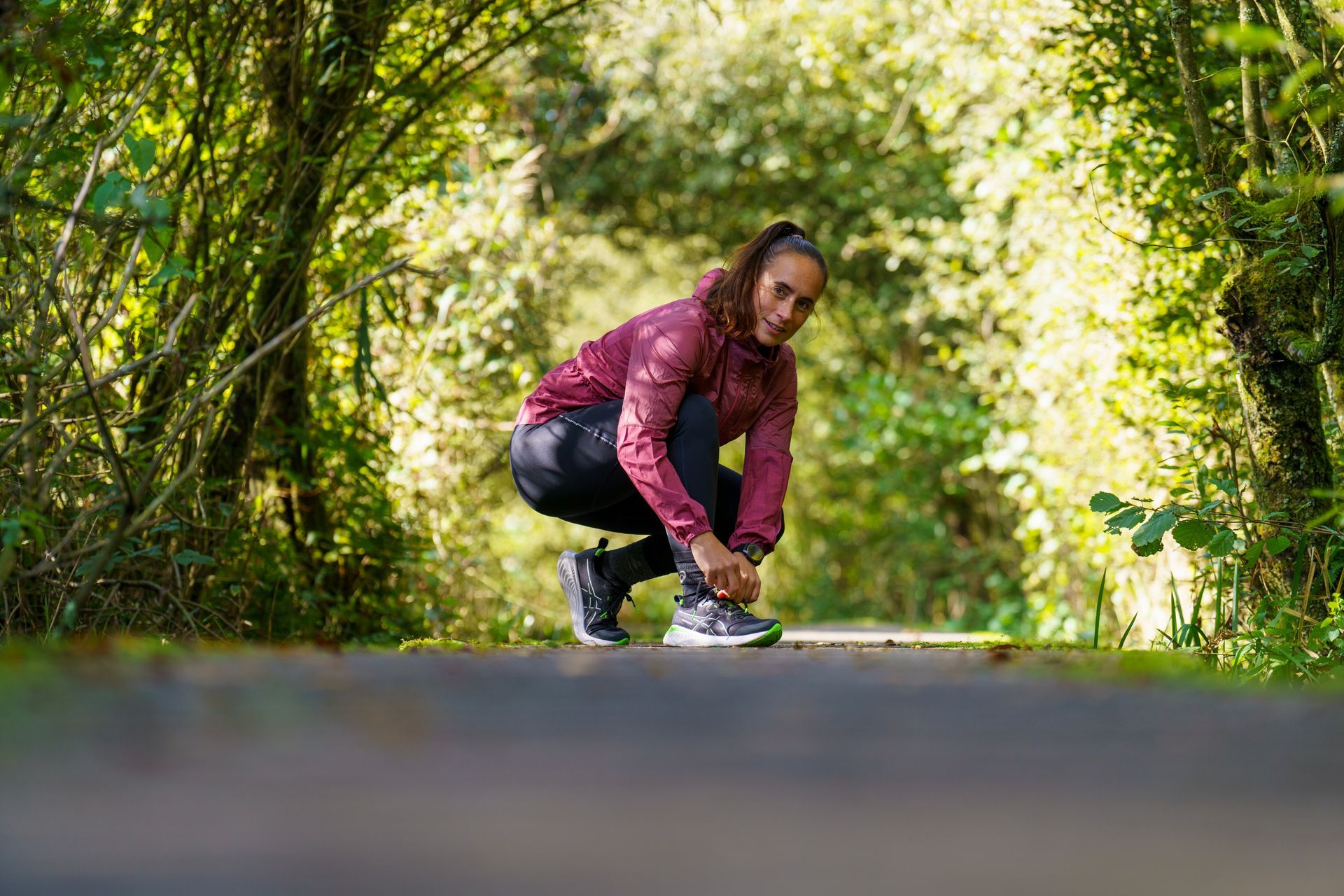 Een vrouw strikt haar schoenen op een weg in het bos.