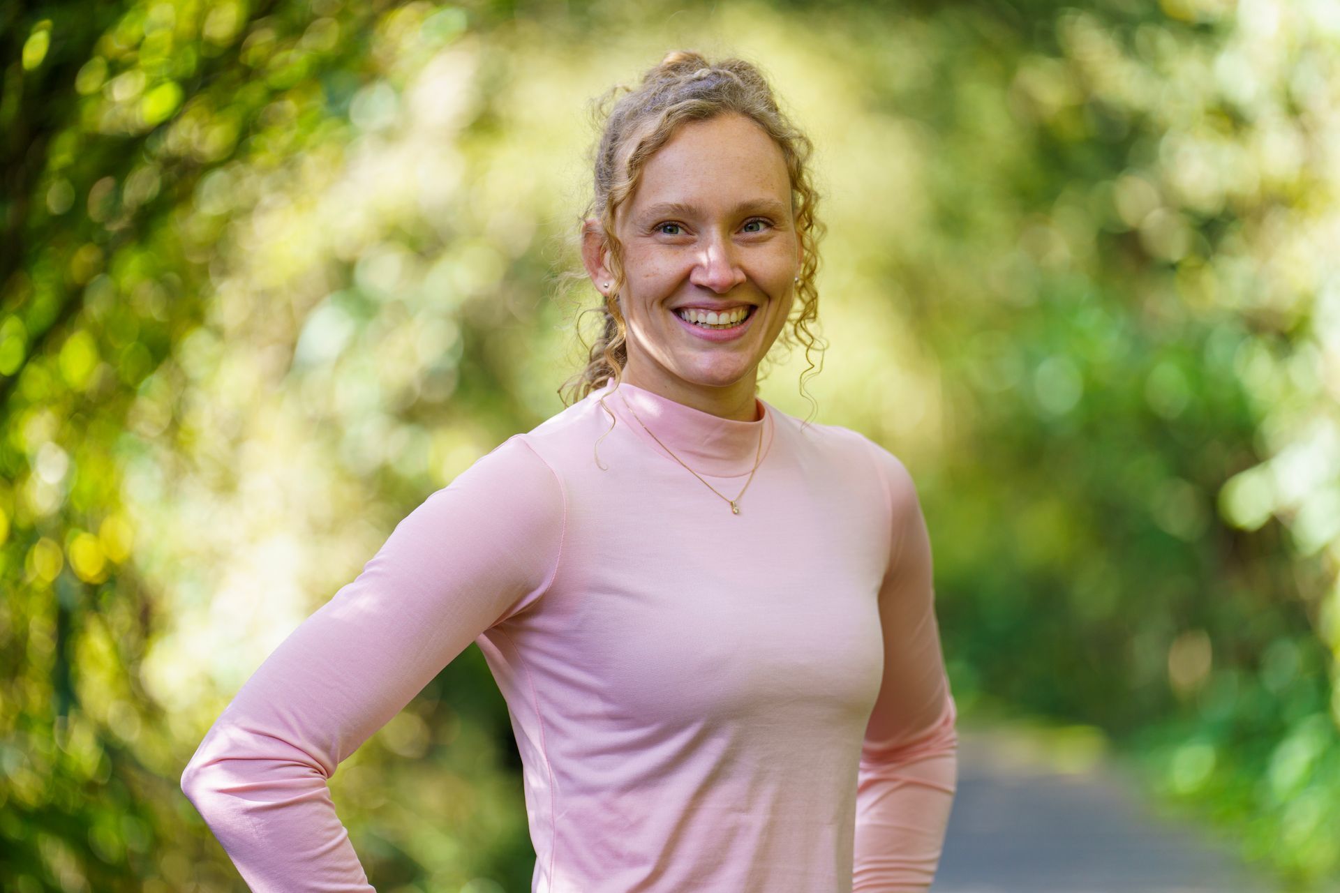 Een vrouw in een roze shirt staat op een pad met haar handen in haar zij.