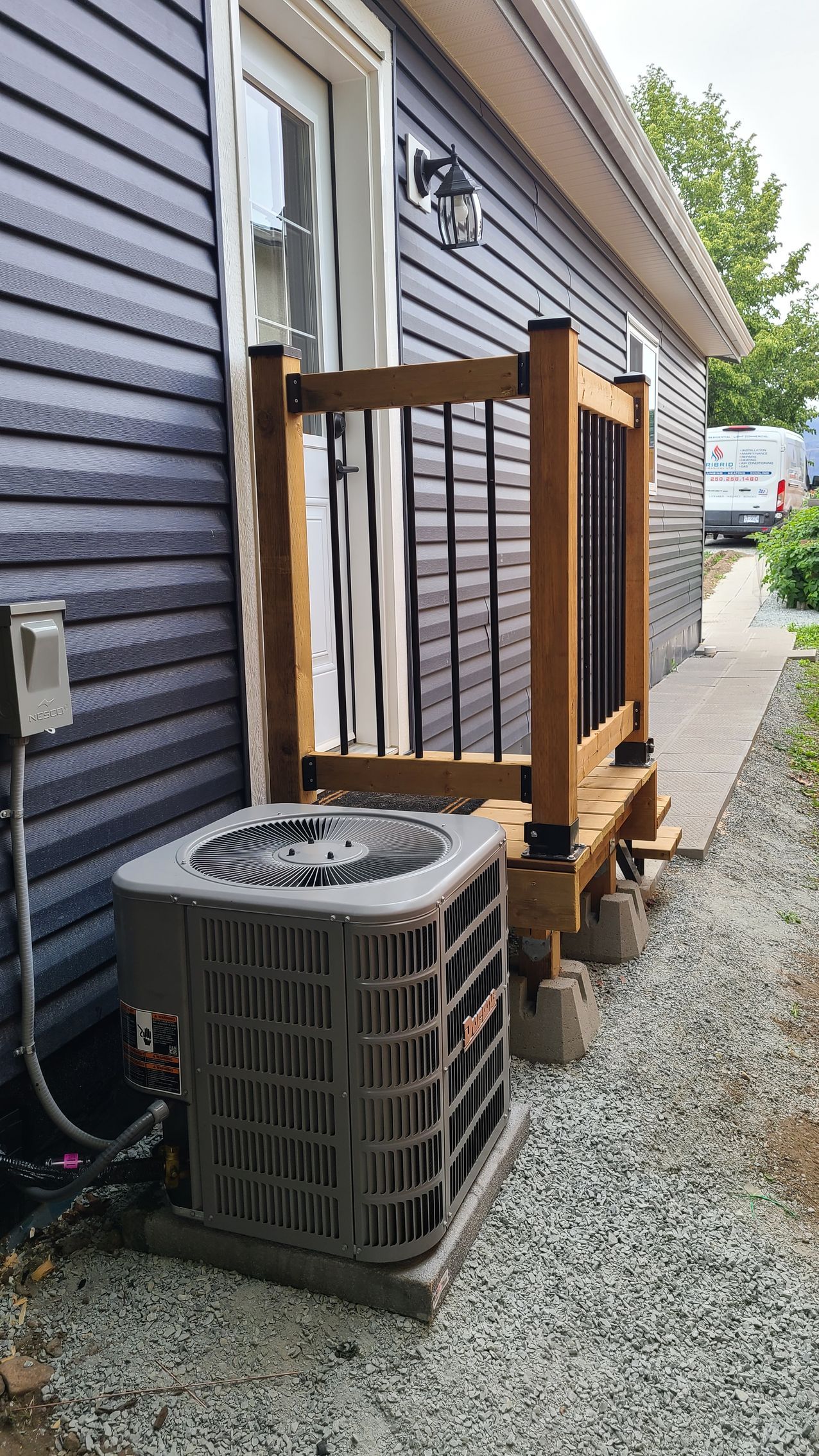 An air conditioner is sitting on the side of a house next to a porch.