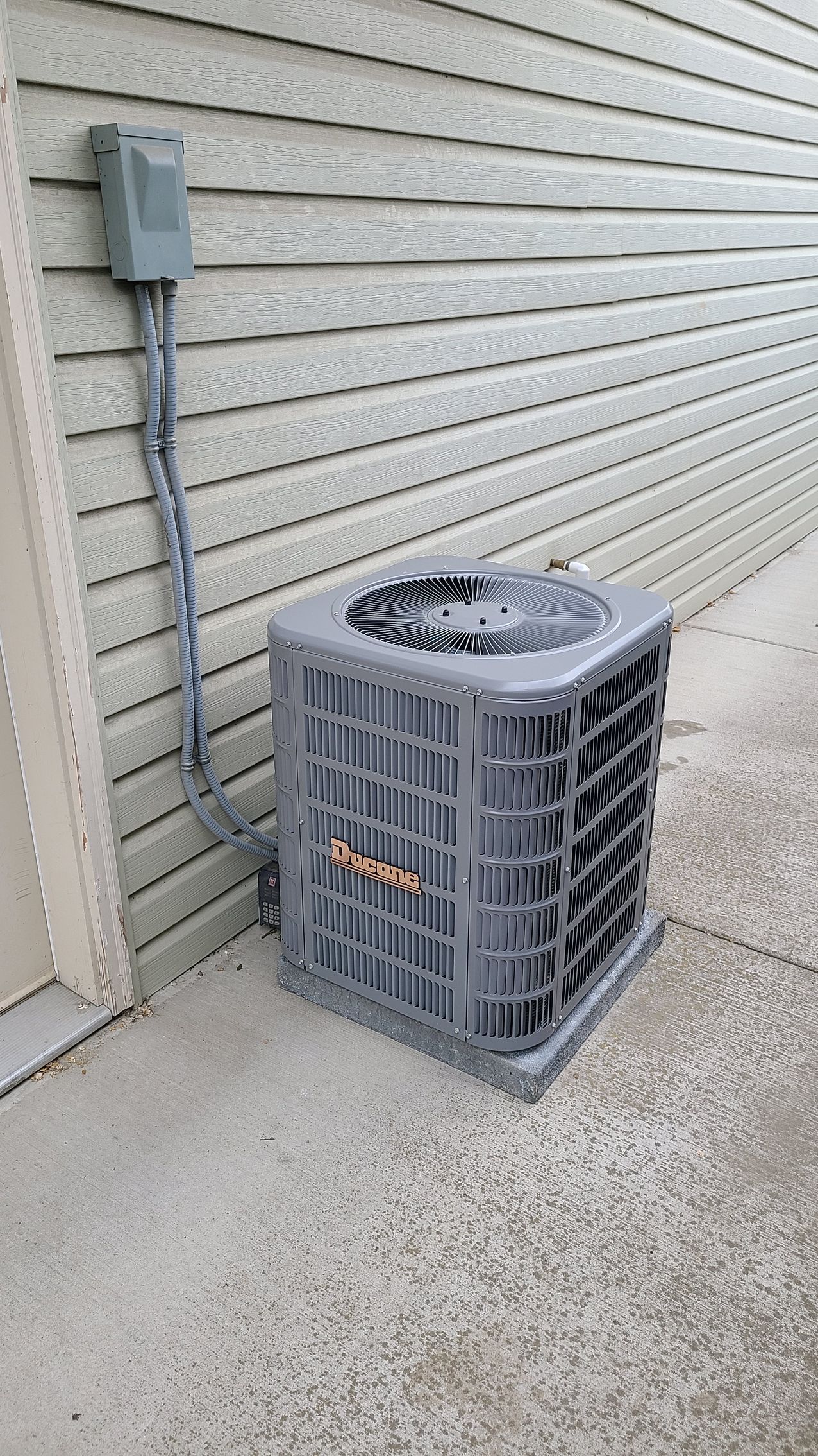 A gray air conditioner is sitting on the side of a building.