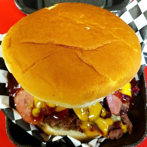 A hamburger with beef , cheese , mustard and barbecue sauce on a bun in a styrofoam container.