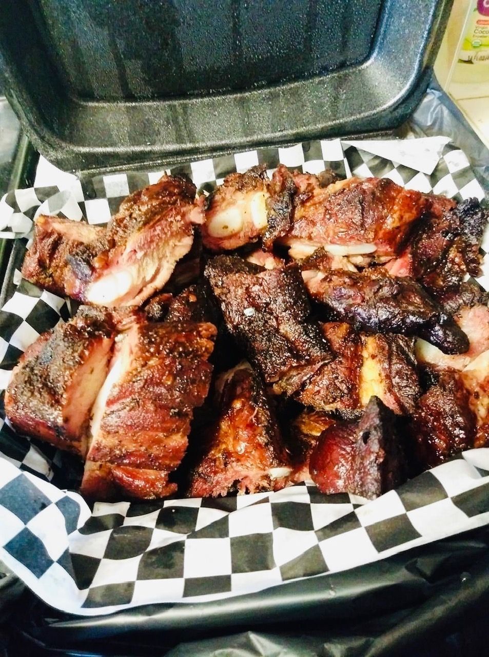 A styrofoam container filled with ribs on checkered paper.