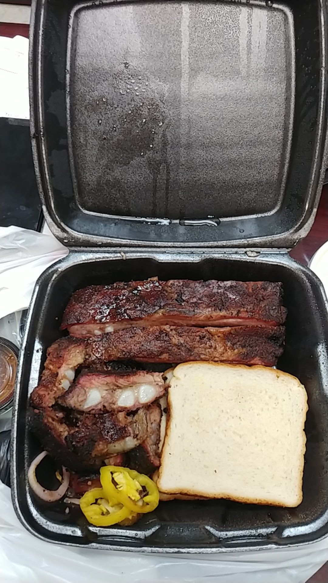 A plastic container filled with ribs , bread and peppers.