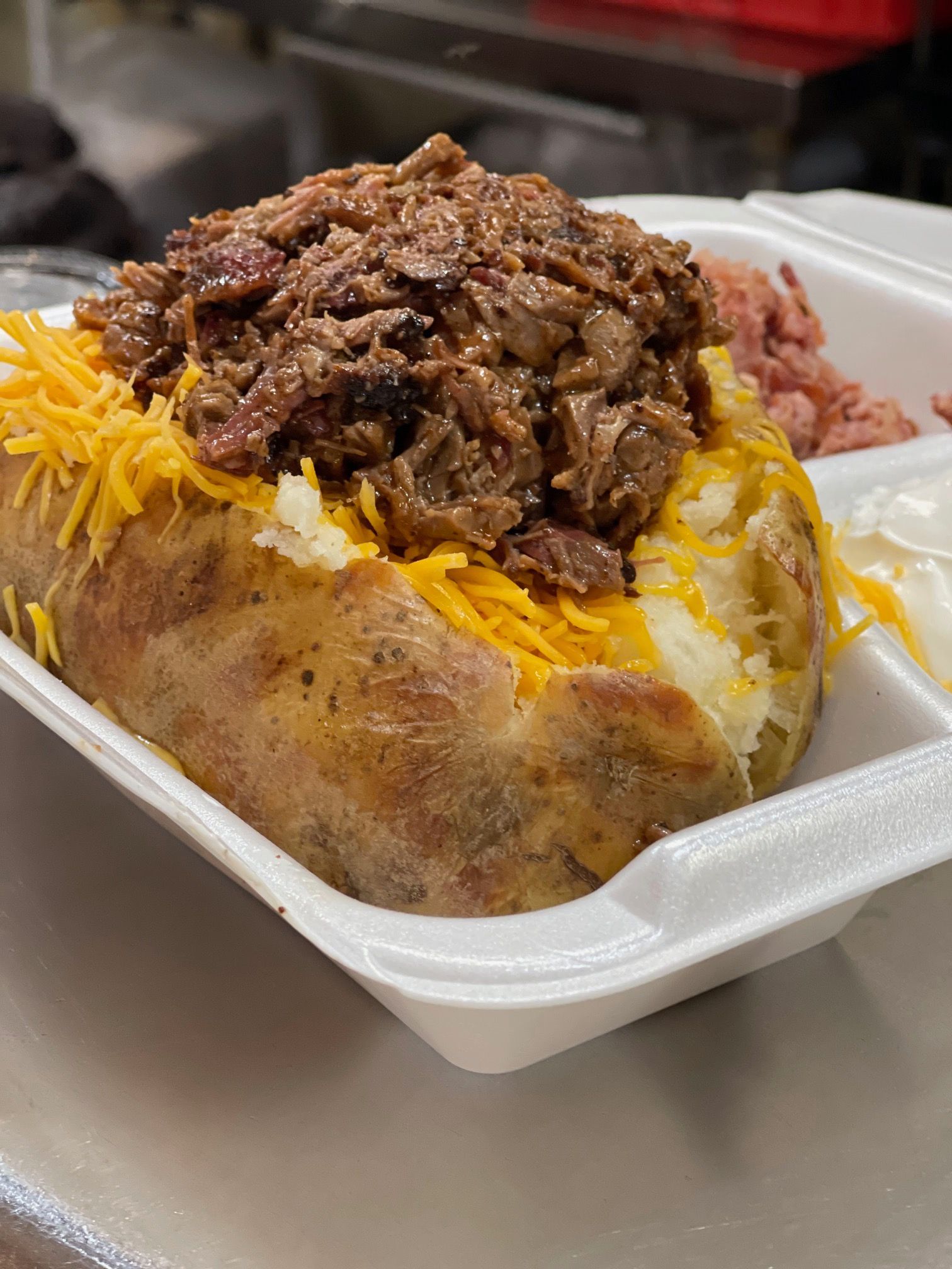 A baked potato filled with meat and cheese in a styrofoam container.