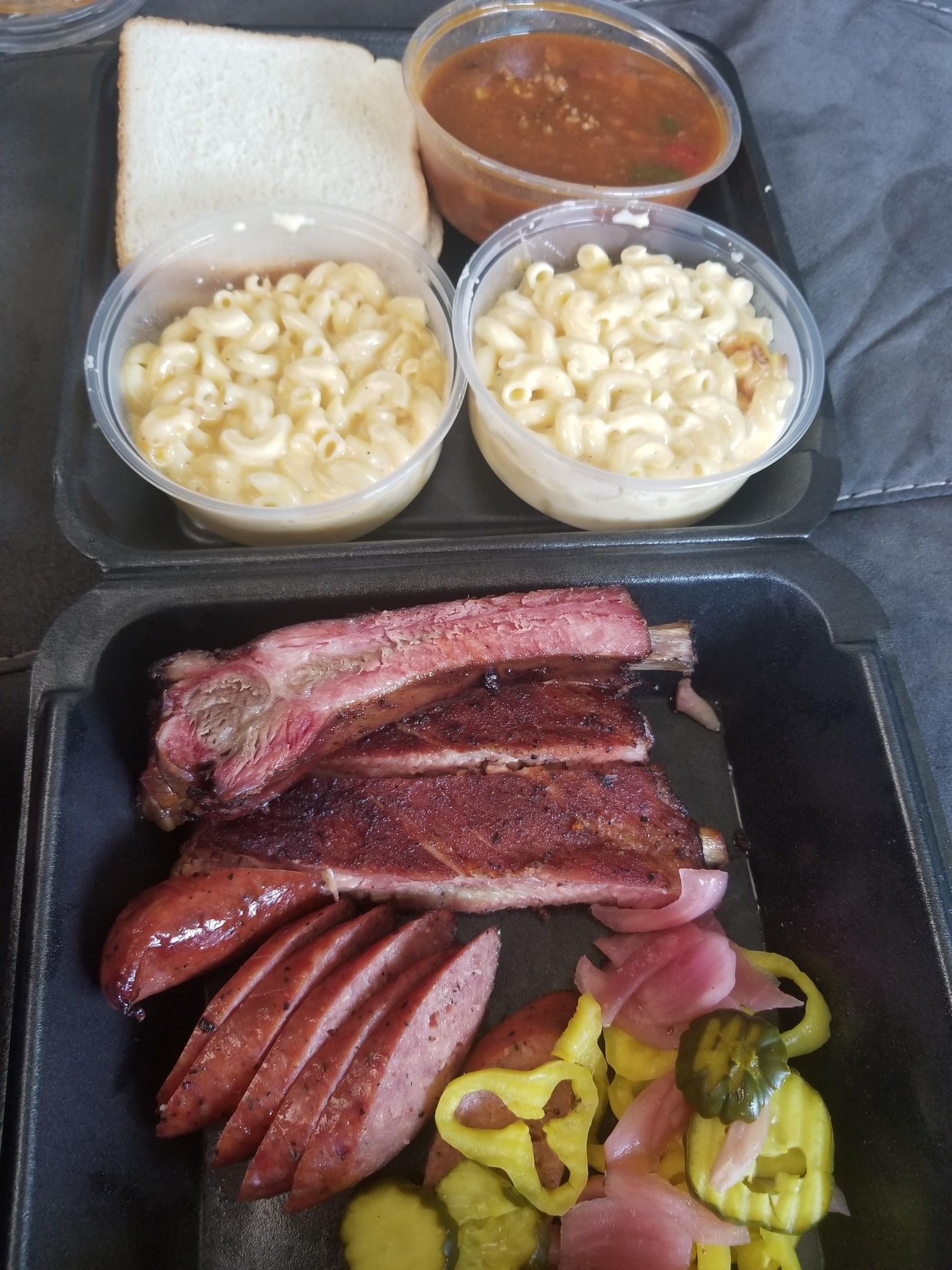 A tray of food with ribs , sausage , macaroni and cheese , and pickles.