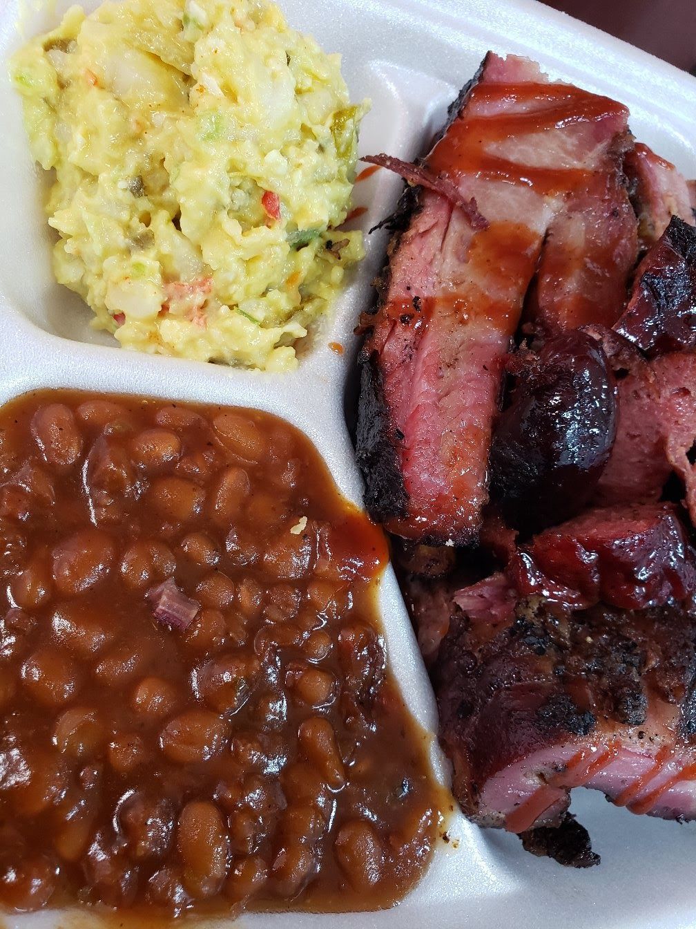 A styrofoam tray filled with meat , beans , and coleslaw.