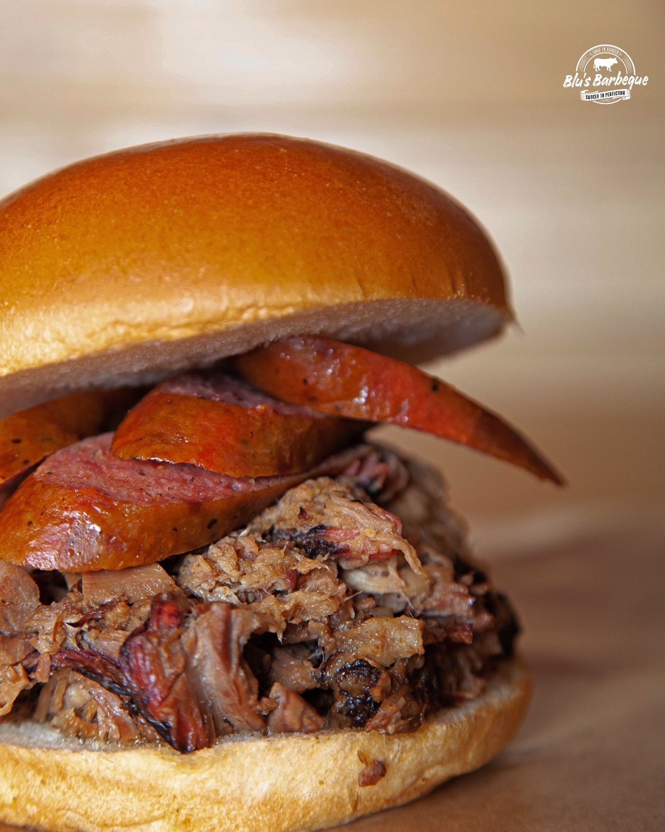 A close up of a sandwich with meat and sausage on a bun on a table.