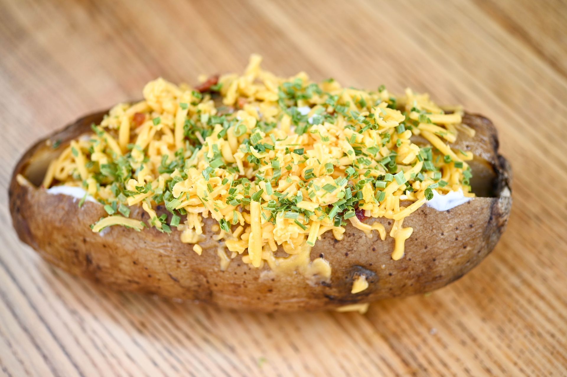 A baked potato covered in cheese and parsley on a wooden table.