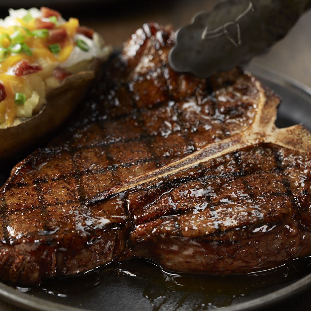 A close up of a steak on a plate with tongs