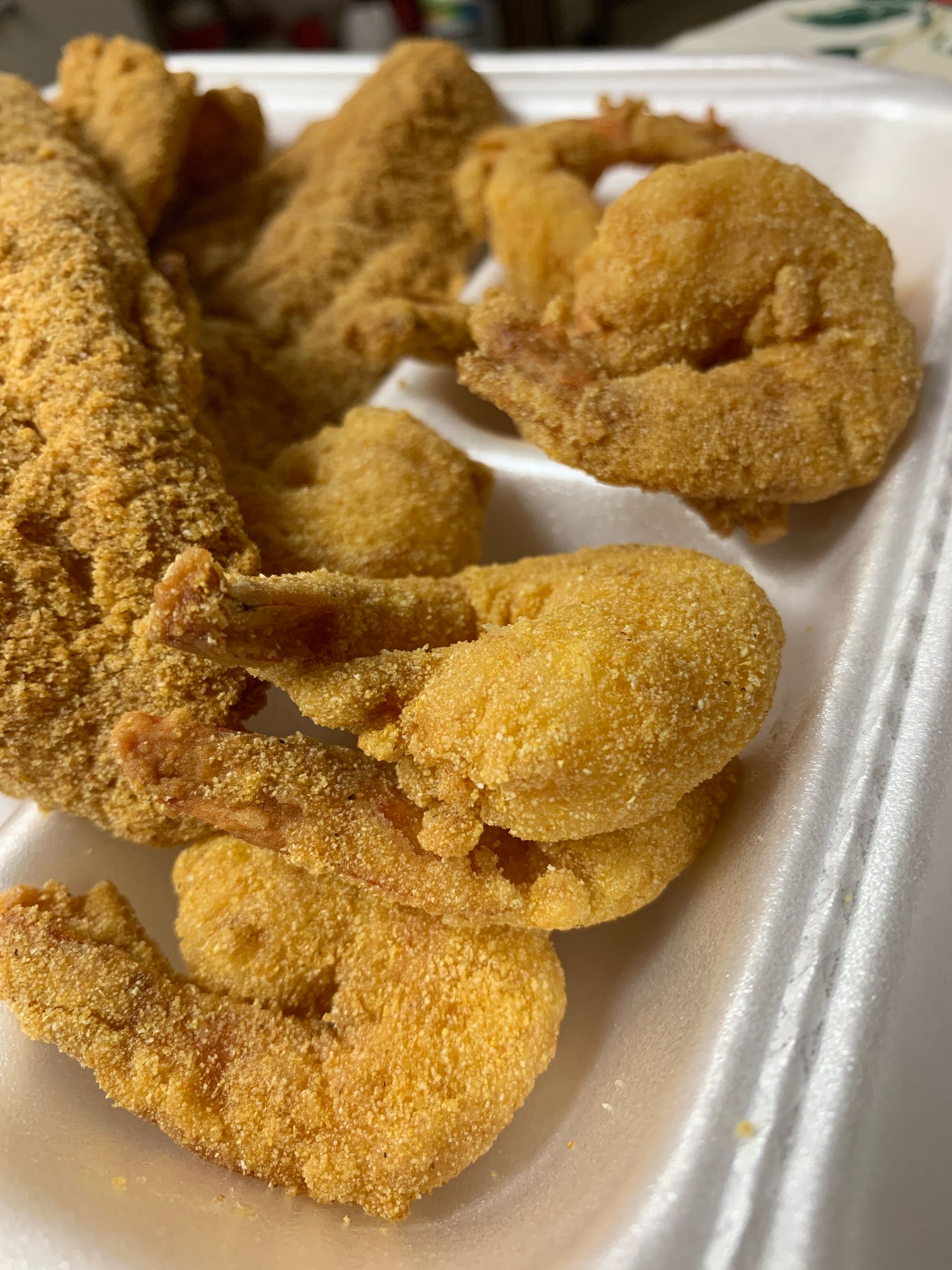 A styrofoam container filled with fried shrimp and fish.