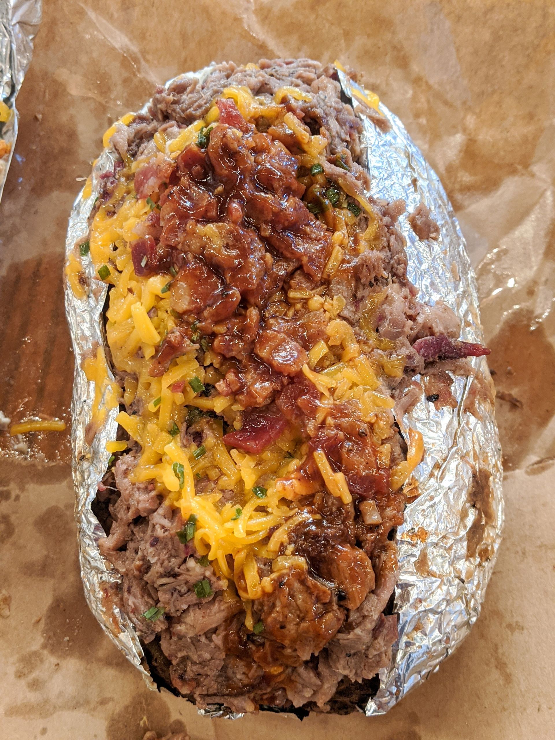 A baked potato with meat , cheese and bacon on it