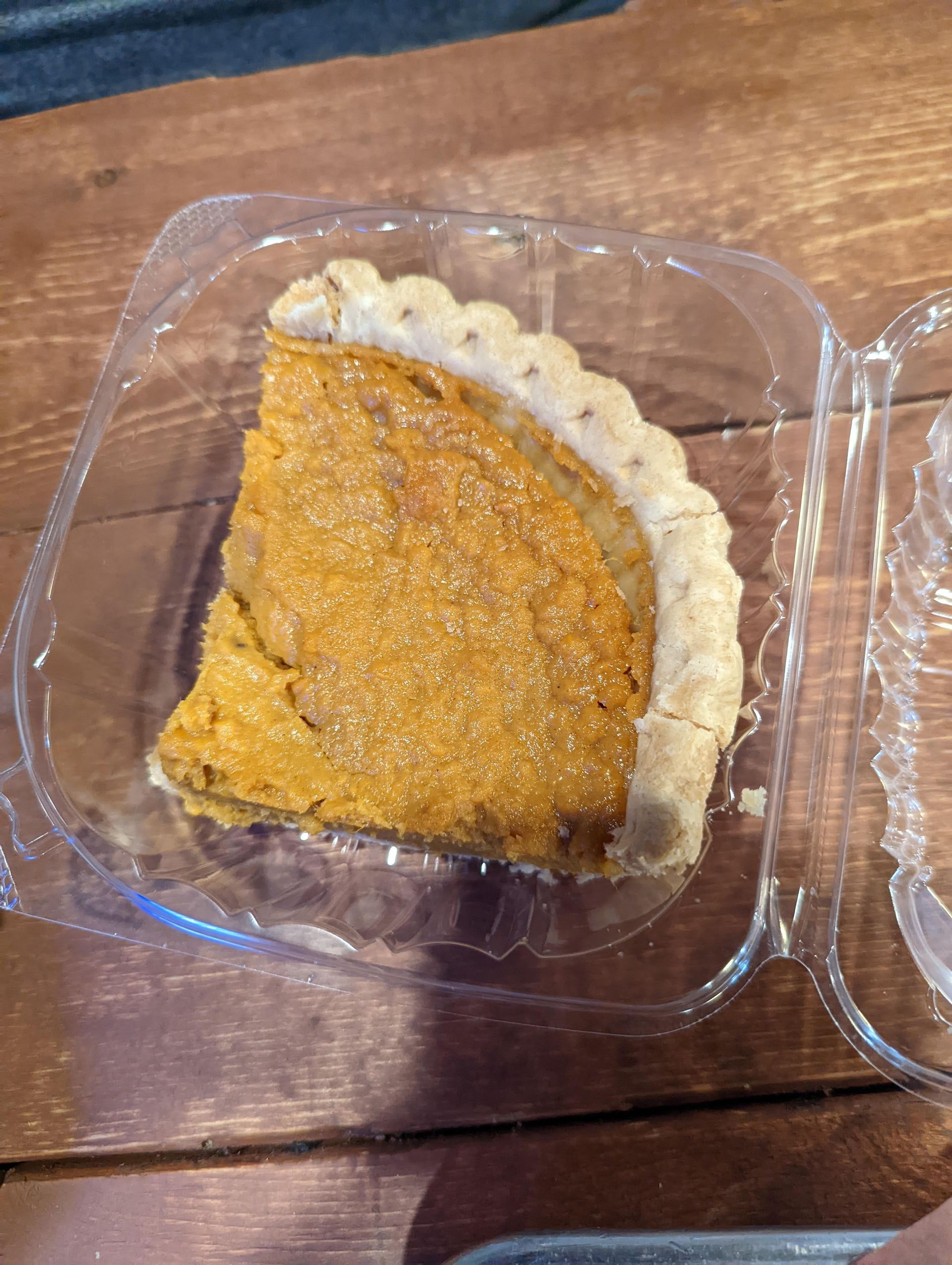 A slice of pie is in a plastic container on a wooden table.