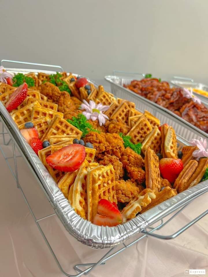 A tray of waffles , chicken , and fruit on a table.