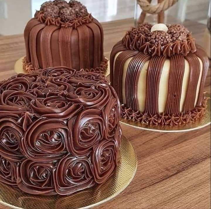 Three chocolate cakes are sitting on a wooden table.