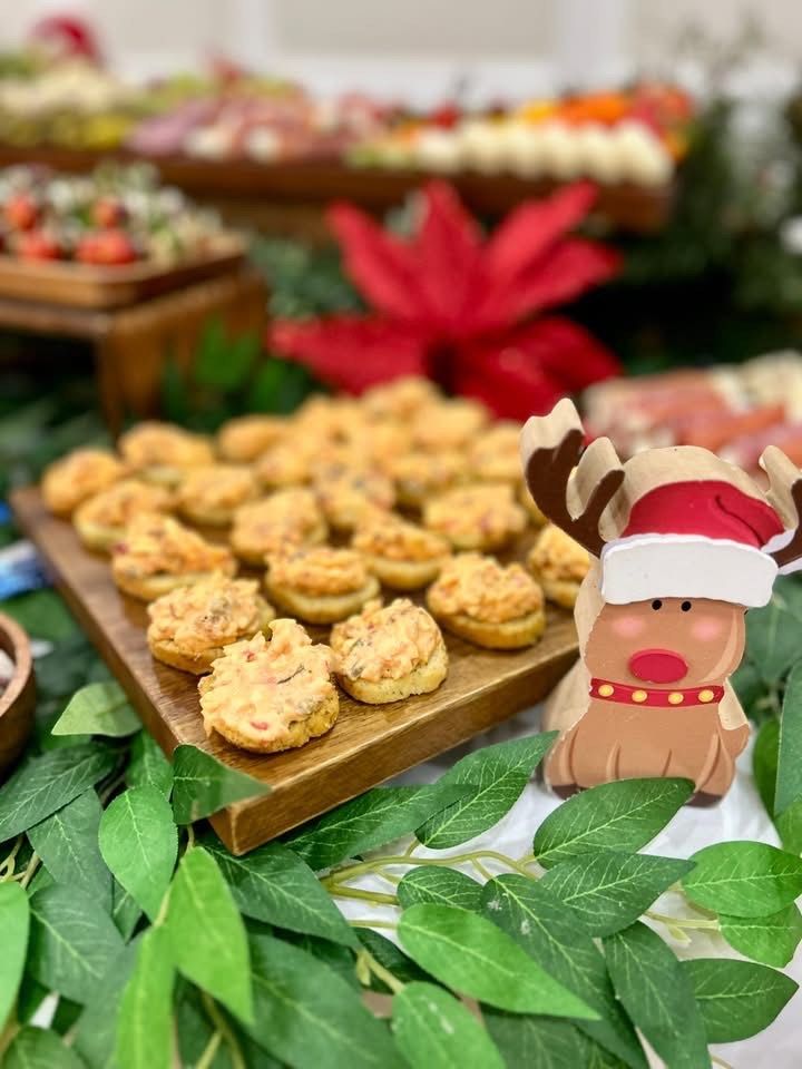 Wooden platter with green grapes, red cranberries, celery, and chocolate. Other food items in the background.